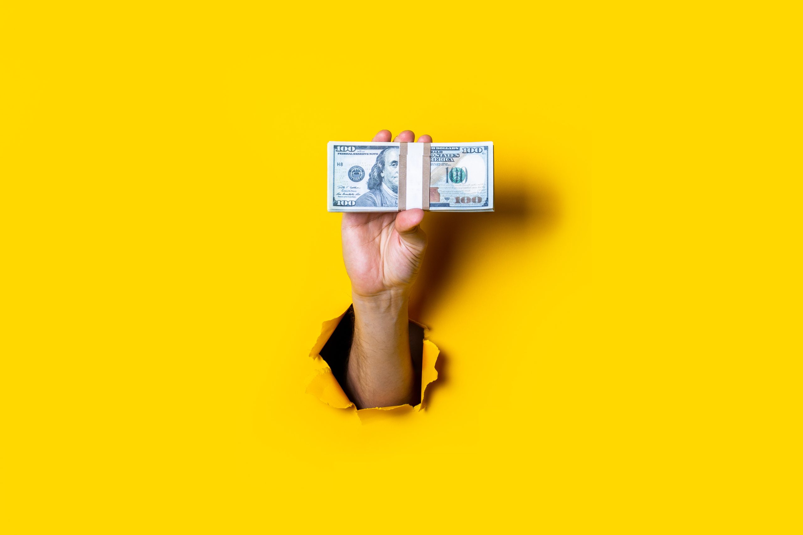 Female hand holds horizontally a bundle of money bills on a yellow background.