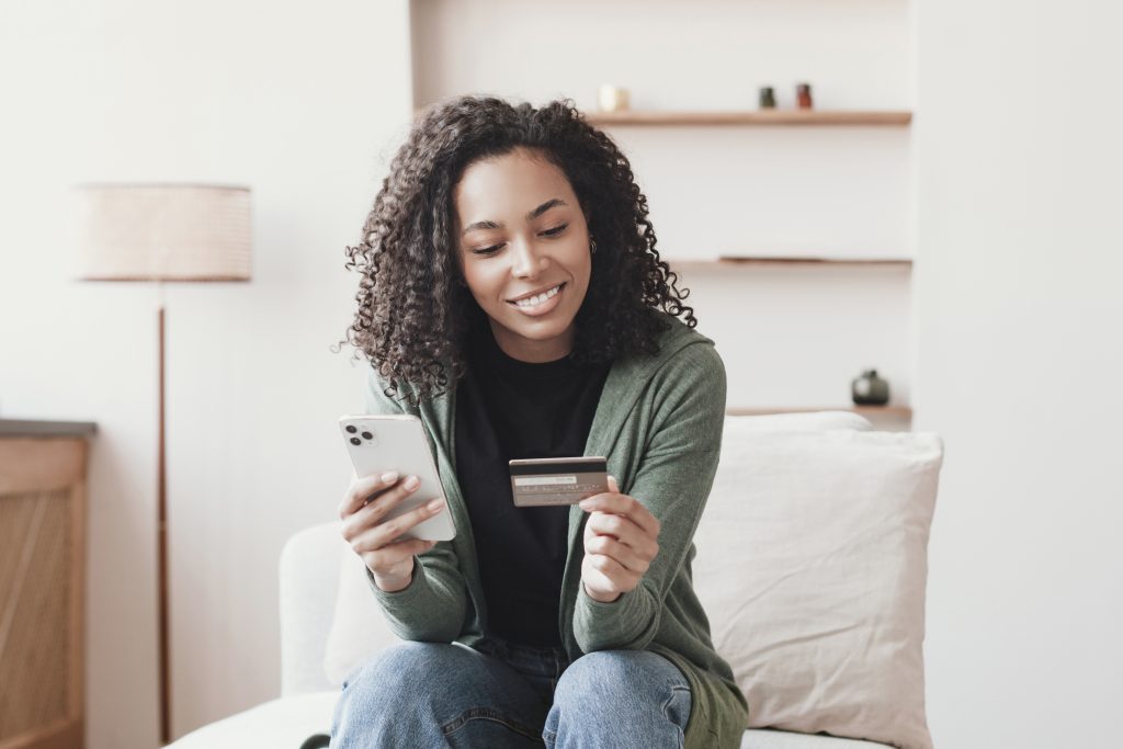 Woman holding credit card and using smartphone at home, business